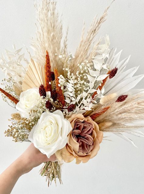 Product Details This Beautiful Bridal Bouquet includes a pretty mix of faux silk Roses & Orange Pinion Grass, Brown Phalaris, Palms, Pampas Grass, White Ruscus and Gypsophila. The Burnt Orange Range rusty, earthy tones are perfect for late Summer & Autumnal boho weddings. Please note flowers may vary slightly in shape/colouration. For wedding orders I can happily share photos first. Flower Colours Orange, Brown, Whites Bouquet Height Roughly 45cm Wrapping Gift wrapped included Each of our bouquets are carefully hand picked and gift wrapped to best match our shop images. This is also a sustainable product that requires no watering. Burnt Orange Flowers Bouquet, Bride Bouquets Burnt Orange, Burnt Orange And Pampas Wedding Flowers, Neutral Bridesmaids Bouquets, Rustic Autumn Wedding Flowers, Black White And Burnt Orange Wedding, Dried Grass Bouquet, Rust Orange Flowers, Autumn Dried Flower Bouquet