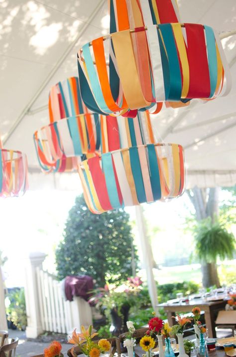 Colorful ribbon chandeliers hang from a white frame tent above farm tables with brightly colored flowers Diy Ceiling Decorations Party, Cellophane Backdrop, Colorful Outdoor Party, Garage Party Ideas, Festival Party Decorations, Party Rental Ideas, Colorful Party Decorations, Ribbon Chandelier, Paper Party Decorations