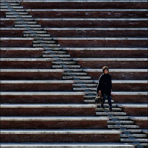 Element: Lines. This image showcases many different lines. There are both horizontal and diagonal lines and there is variation in the spaces between the two sets of horizontal lines. The woman in the corner stands draws attention in the image due to her lack of straight lines, making her the focal point. Line In Photography, Lines In Photography, Symmetry Photography, Photography Elements, Line Photography, Image Composition, Photography Assignments, Photo Elements, Pattern Photography