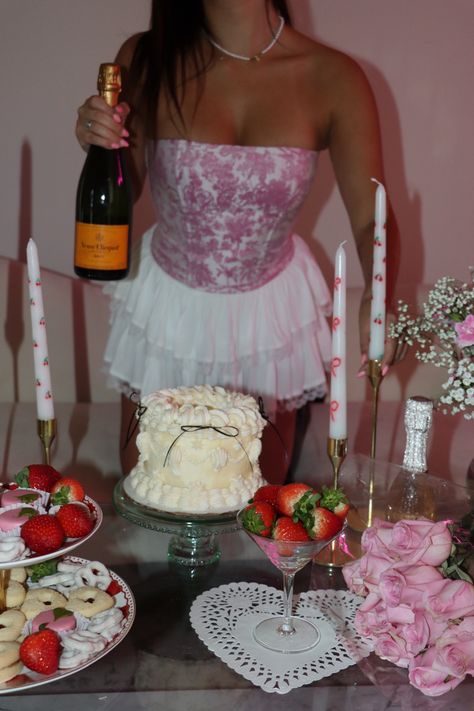 Girl shot from the neck down holding a bottle of champagne. In front of her is a cute birthday party setup with coquettish cakes, candy, strawberries, and candles. Soft Party Aesthetic, 28th Birthday Aesthetic, Light Pink Party Aesthetic, Birthday Valentines Theme, 20 Bday Party Ideas, Pink Cake With Cherries, Pink And Red Birthday Party Decor, Cherry Birthday Party Theme, Cute Aesthetic Cake