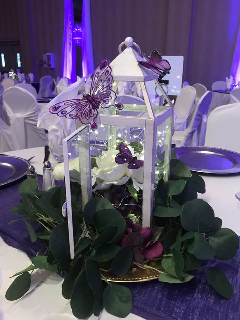 Butterflies in the Lilacs; lovely garden centrepieces for this wedding #lethbridgeeventrentals #lethbridgeevents #wedding #weddingreception #lilac #purple #garden #butterflies #centrepiece #lantern #uplight #backdrop #headtable #weddingdecor Centerpieces For Quince Purple, Lilac Wedding Centrepiece, Purple Butterfly Quinceanera Centerpieces, Butterfly Centerpiece Ideas Wedding, Quinceanera Purple Centerpieces, Lilac Table Centerpieces, Purple Quince Butterfly Theme, Butterfly 15 Theme Centerpiece, Enchanted Forest Centrepiece