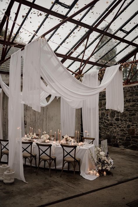 Minimalistic, neutral wedding reception room with glass roof, white wedding drapes, tapered candles and white rose and foliage decorations | Sam Sparks Photography | <a href="https://www.rockmywedding.co.uk/ceiling-drapes-decoration">See more of this real wedding</a> Roof Draping Ideas, Romantic Decor Wedding, Wedding Roof Draping, Linen Drapes Wedding, White And Candle Wedding, Drapes Ceiling Wedding, Fabric Drapes Wedding, Wedding Ideas Industrial, All Candle Wedding Reception