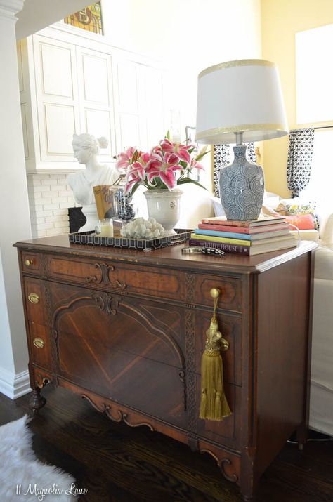 While painted furniture is still incredibly popular, don't overlook the beauty of dark wood.  We used this vintage dresser as a grounding point in a living room filled with white slipcovered furniture, and it provides a wonderful contrast (plus, those drawers are oh-so-useful for storing table linens).  Then we hit HomeGoods for everything we needed to style the top--a blue and white lamp, tray, apothecary jar, plaster bust, and more--and make it a functional and beautiful focal point {sponsored Antique Wood Furniture Living Room, Painted Furniture In Living Room, Dark Sideboard Decor, Vintage Dresser In Living Room, How To Style A Side Table Living Rooms, Table Top Decor Living Room, Styling Dark Furniture, Vintage Living Room Decor Antique, Dining Room Side Board Decor