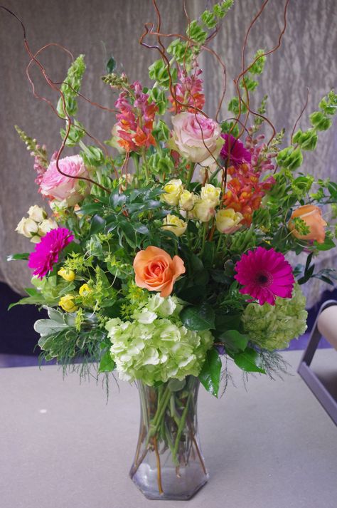 Tall vase arrangement featuring gerber daisies, hydrangeas, long-stem roses, spray roses, bells of Ireland, snapdragons, bupleurum, and curly willow. Tall Vase Arrangements, Tall Floral Arrangements, Bouquet Champetre, Arrange Flowers, Spring Flower Arrangements, Plantas Bonsai, Fleurs Diy, Spring Floral Arrangements, Church Flower Arrangements