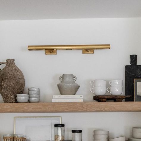 Visual Comfort & Co. on Instagram: "Shelfie appreciation post. 😍 Designer @rachaelbialkowski of @thelifestyledco⁣⁣⁣⁣⁠ helped her client @suzannavilla create a fresh yet timeless kitchen using a mix of neutral millwork and organic elements. Selected by the homeowner, the "cookies and cream" backsplash and countertop make a bold statement while pairing gorgeously with the white oak shelves for a natural look. Overhead, our iconic 30" Cabinet Maker's Picture Light by Chapman & Myers adds classic appeal to the space in a radiant Hand-Rubbed Antique Brass finish. The fixture brings a soft glow to the thoughtful collection of entertaining necessities and artful objects below. ​Architect: @harrisondesign 📷: @elizabethlaurengranger" Lights Over Open Shelves In Kitchen, Lights Above Floating Shelves In Kitchen, Picture Lights In Kitchen, Picture Light In Kitchen, White Oak Shelves, Cream Backsplash, Kitchen Built Ins, Brass Picture Light, Lamp Kitchen