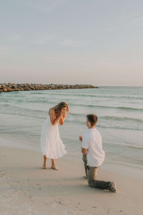 Young couple dressed in white & neutral summer clothing - on shore of beach in St Andrews State Park, PCB Florida.  Young man is kneeled down on one knee, with ring outstretched, girl is excitedly covering her face with her hands. Photo taken by intimate wedding & portrait photographer Brittney Stanley of Be Seen Photos Propose On The Beach, Simple Proposal Ideas Beach, Surprise Beach Engagement, Florida Proposal Ideas, Beach Proposal Ideas Simple, Engagement Photos Sunset Beach, Boyfriend Beach Aesthetic, Proposal Beach Photos, Engagement On Beach