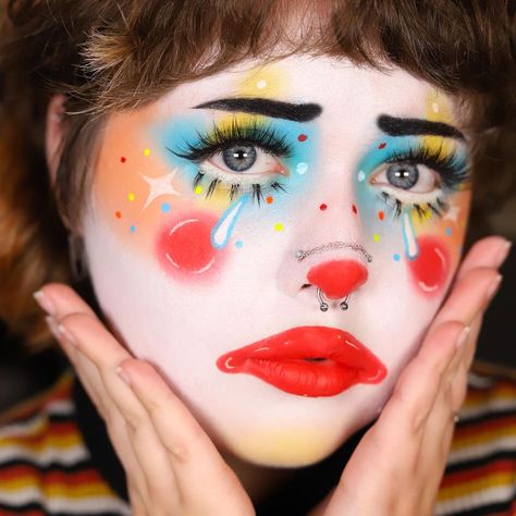 This look radiates joy and whimsy with its vibrant color palette. The artist has used a white base and adorned the face with multicolored accents, including blue eyeshadow, yellow blush, and red lips. The dramatic eyelashes and dotted patterns on the cheeks and around the eyes add a playful, colorful touch. The red clown nose and subtle glitter create a cute yet simple appearance, making this look both eye-catching and approachable. This inspiration is perfect for anyone looking to bring a burst of color and creativity to their clown makeup repertoire.   Photo credit by: @katie.artistry Couple Clown Makeup, Colorful Clown Makeup, Clown Makeup Ideas, Eyeshadow Yellow, Clown Makeup Tutorial, Dramatic Eyelashes, Cute Clown Makeup, Circus Makeup, Halloween Makeup Clown