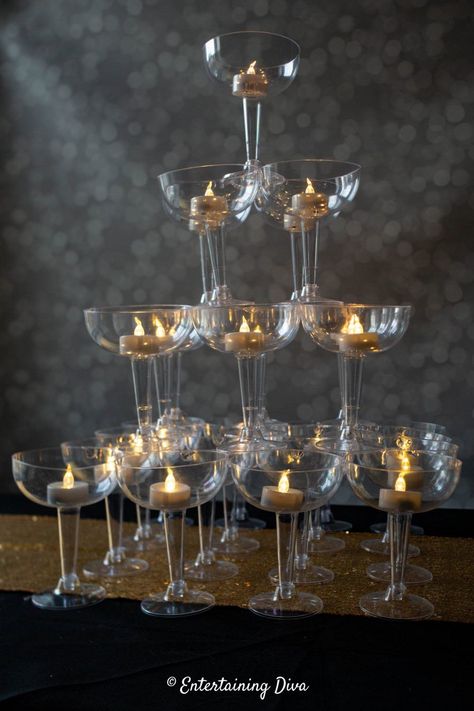 This DIY champagne glass tower is made from plastic coupe glasses that are glued together so it won't fall over or break! It makes a great centerpiece for a Great Gatsby party, roaring 20's event or speakeasy. #entertainingdiva #gatsbyparty #roaring20s #speakeasyparty #centerpiece  #diypartydecor Great Gatsby Centerpieces, Champagne Glass Tower, Gatsby Centerpieces, Great Gatsby Decorations, Roaring 20s Party Decorations, 20s Party Decorations, Gatsby Decorations, Deco Nouvel An, Gatsby Birthday Party