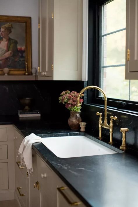 A kitchen with off-white cabinets, black marble countertops, and an ornate brass faucet Black Counter Farmhouse Kitchen, Casa Casuarina, Interiors 2023, Soapstone Counters, Ohio House, 1920s House, Bistro Furniture, Butlers Pantry, Timeless Kitchen