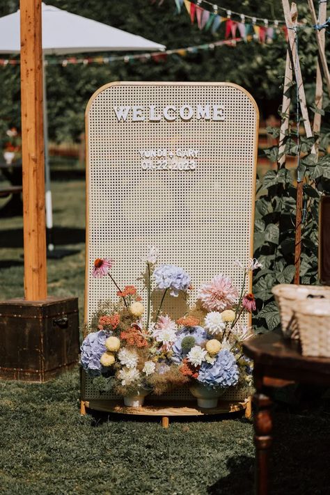 charming rattan wedding welcome sign with pastel primary color floral arrangements for a sunny outdoor ceremony Brides 2024, Bespoke Decor, Wedding Entrance Sign, Wedding Ceremony Decorations Outdoor, Minimal Contemporary, Wedding Entrance Decor, Floral Signs, Colourful Wedding, Wedding Brides