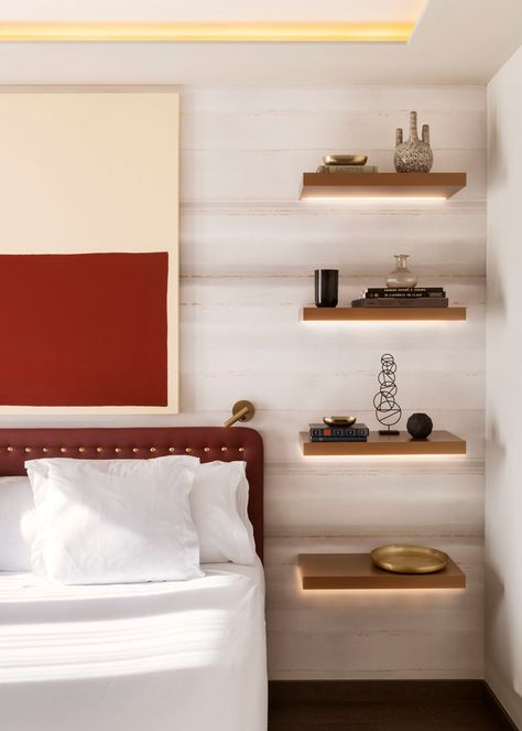 In this modern bedroom, four floating wood shelves with hidden lighting have been installed, with the lowest shelf at the correct height for a bedside table, while the other three shelves have been used to display decorative items. #BedroomDesign #BedsideTable #InteriorDesign #Shelving Bedside Wall Shelf Ideas, Floating Shelves As Bedside Tables, Wall Shelf Bedside Table, Shelf In Bedroom Wall, Floating Lights Bedroom, Bedside Night Stands Ideas, Bedroom Floating Shelves Night Stand, Shelves As Bedside Tables, Floating Night Stand Ideas Bedrooms