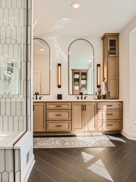 Go to the link to see more of this stunning primary bathroom remodel. This custom vanity was built for beauty and tons of storage. Long arched mirrors and linear sconces. Black matte plumbing fixtures. Open glass doors on the top cabinets to display decor. Modern Scandinavian style. Black wood herringbone tile floors Master Bath With Oak Cabinets, Oak Bathroom Vanity Modern, Bathroom Remodel Light Wood Cabinets, Tall Mirror Bathroom Vanity, Long Mirrors In Bathroom, Master Bath Storage Cabinet, Bathroom Arch Mirror Ideas, Master Bath Long Vanity, White Bathroom Oak Vanity