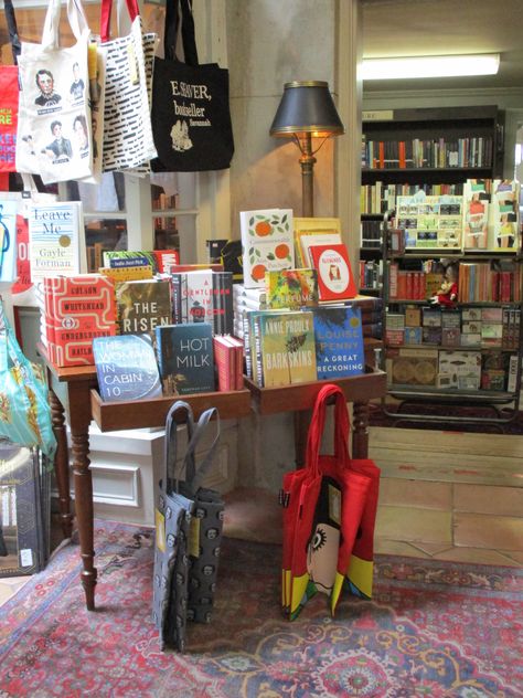 This little table display at E. Shaver Booksellers is in a key location between rooms. This repurposed desk makes a quaint statement, especially with the lamp, literary totes, and display of the week's newest book releases. Book Display Ideas Retail, Book Shop Display Ideas, Book Display Store, Small Book Store Ideas, Diy Book Display Stand, Pop Up Book Store, Retail Book Display, Book Display Table, Book Store Display Ideas