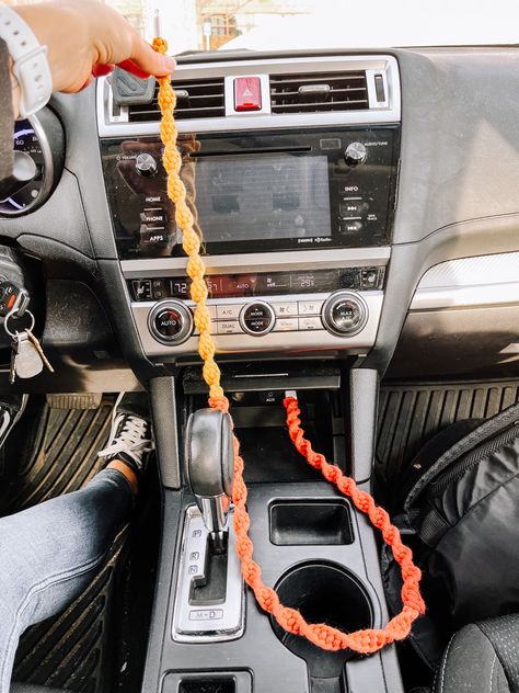 A bright-colored macrame phone charger plugged into the USB port inside a car. Color of phone charger is called sunburst which is an ombré style of red fading to yellow Country Car Decorations Interior, Car Boho Interior, Diy For Car Decor, Car Inspo Interior Boho, Summer Car Interior, Boho Car Aesthetic, Car Mirror Hangers Diy, Fall Car Accessories, Organized Car Aesthetic