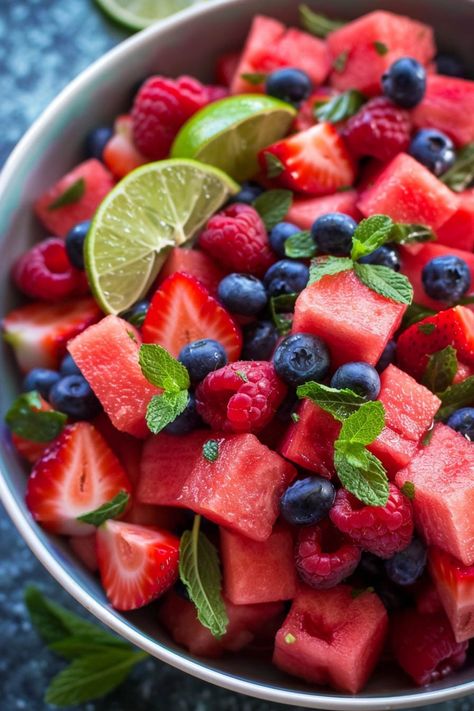 A vibrant bowl of mixed fruit salad with watermelon pieces, strawberries, blueberries, raspberries, garnished with fresh mint leaves and a lime wedge. Fruit Salad Bowls Ideas, Diced Fruit Salad, Pretty Fruit Salad, Mojito Fruit Salad, Small Fruit Salad, Summer Salad With Fruit, Summer Meals Aesthetic, Potluck Healthy Recipes, Fruit Salad Mexican Style