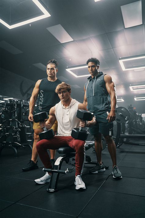Three TLF influencer and fitness models in TLF gym HQ. All decked out in TLF new League Collection for men. Featuring colors of Unbleached, Garnet, Armada, Brass, and Black. They are sitting on the bench and holding large weights ready to get to work and lift. The epic lights and apparel make for a great workout in the gym.