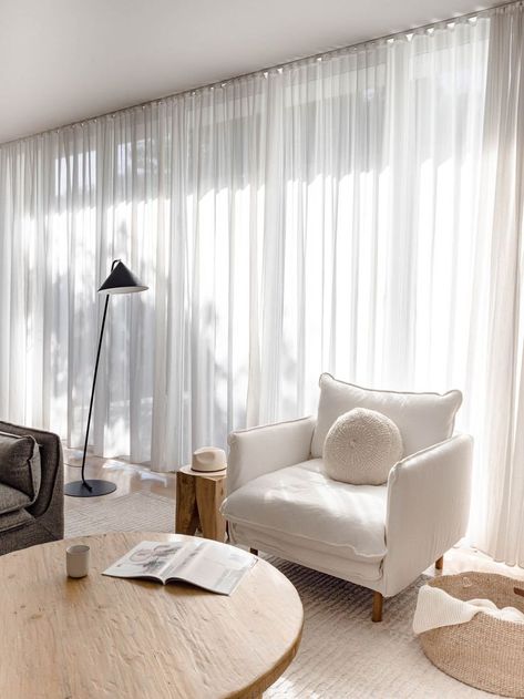 Neutral living room with a relaxed and coastal vibe. The white linen armchair, old elm wood coffee table, black floor lamp, sheer curtains and jute throw basket make this space layered in textures. Click to see more photos of this living room! Sheer Curtains Living Room Coastal, Living Room Curtains Linen, Black Floor Lamps Living Room, Modern White Curtains Living Room, Cream Sheer Curtains, Linen Sheers In Living Room, White Linen Sheer Curtains, Off White Sheer Curtains, Curtains Living Room Minimalist