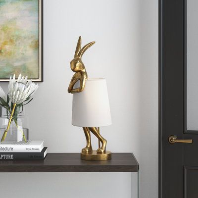 Brighten up your home with this distinctive table lamp and have this figurine ready for Easter time entertaining. Crafted from resin, this sculptural piece is a statue of a rabbit on its hind legs, eyes closed, and with a slightly leaning posture. A glam gold finish brings a luxe look to the overall design, and it has an in-line switch for easy turning on and off. The rabbit is holding up a white linen empire shade to hide and a 25W max bulb (sold separately). At 27" tall and only 9" across, thi Figurine, Gold Rabbit, Desk Lamps Bedroom, Rabbit Lamp, Novelty Lamps, Linen Lamp Shades, Touch Table Lamps, Touch Table, Gold Table Lamp