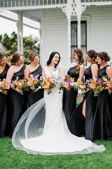 Bride with bridesmaids in black gowns with colorful bouquets Pastel, Black And White Weddings With A Pop Of Color, Black Bridesmaids Dress Colorful Flowers, Summer Wedding Colors With Black, Black Bridesmaid Dresses Colorful Shoes, Black And White Wedding With Colored Flowers, Black Bridesmaid Dresses Colorful Bouquets, All Black Wedding With Colorful Flowers, Black With Bright Colors Wedding