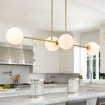 This 4-light kitchen island chandelier will be the best piece of artwork to make you a striking space. It features a clean line design of four lights attached to the horizontal metal bar. There are two finishes of its frame for your choice - matt black or brushed gold and it has white glass globe shades for decor. The linear globe glass chandelier will create a cozy atmosphere for your dining room, kitchen island, and any other place in your home. Finish: Brushed Gold | Mercer41 Oswal 4 - Light Modern Kitchen Island Chandeliers, Island Lighting White Kitchen, Globe Pendant Lights Over Kitchen Island, Brass Globe, Lights Over Kitchen Island, Glass Globe Chandelier, Kitchen Table Lighting, Pendant Light Set, Bar Chandelier