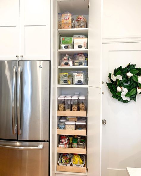 This vibrant kitchen features a large stainless steel refrigerator and bright white cabinets adorned with a leafy wreath. A narrow pantry is built into the wall and displays rows of clear bins with neat labels. Turn a small space in your kitchen into a pantry with stackable bins and canisters, and use labels to keep everything tidy. Small Pantry For Small Kitchen, Narrow Kitchen Storage Ideas, Small Space Pantry Cabinet, Long Narrow Kitchen Cabinet Storage, Tall Narrow Refrigerator, Narrow Cupboard Ideas, Organisation, Small Pantry Beside Refrigerator, Tall Narrow Pantry Cabinet