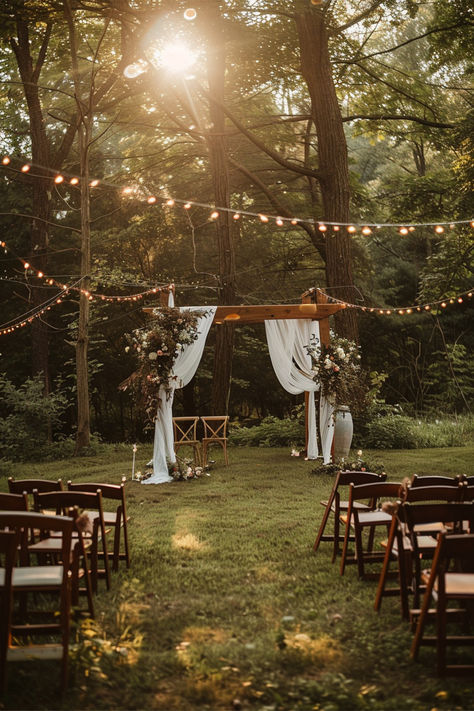 A beautiful garden wedding setup with a wooden arch draped in white fabric and adorned with floral arrangements, surrounded by string lights and wooden chairs under tall trees. Wedding In A Backyard, Forest Backyard Wedding, Gazebo Ideas Wedding Outdoor, Garden Wedding Decor Outdoor Ceremony Reception Ideas, Fall Backyard Reception Ideas, Outdoor Forest Wedding Reception, Outdoor Wedding Tree Lights, Wedding Venues Ideas Outdoor, Low Key Outdoor Wedding