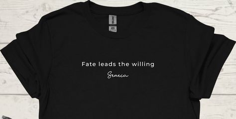 Embrace your destiny with our "Fate Leads the Willing" t-shirt, inspired by the timeless wisdom of Seneca.  This design serves as a daily reminder that life's journey is guided by our openness to its call. Crafted for dreamers and doers, this shirt encourages you to trust the path laid before you and to move forward with courage and grace.  Wear it as a symbol of your inner strength, knowing that fate favours those who are willing to embrace its guidance.  Let your journey unfold with purpose and passion. Crafted from 100% preshrunk ringspun cotton.