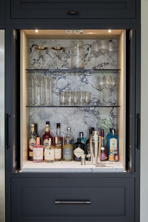 Here's the inside of a bespoke bar unit with pocket doors that fold right back into the cupboard when in use. The backsplash is in Moonrock Quartzite to match the work surfaces in the kitchen and combined with the glass shelves and lighting, create a sophisticated and luxurious drinks area. #kitchendesigns #luxurykitchen #kitchenextension Small Built In Bar Nook, Built In Liquor Cabinet, Small Built In Bar, Alcove Bar, Bourbon Cabinet, Bar Unit For Home, Glass Bar Shelves, Drinks Area, Built In Bar Cabinet