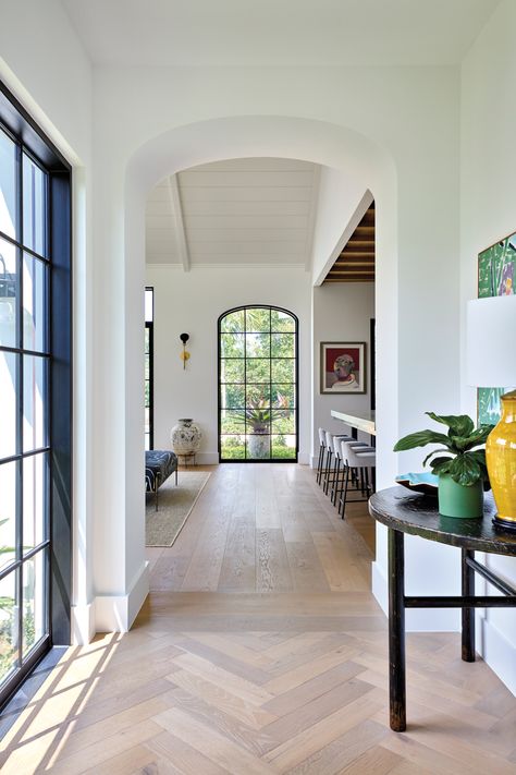 The entry gallery is lined with Provenza Floors’ Napoli European oak from Designer Floors. Beyond, an antique vessel stands beneath The Urban Electric Co.’s Scoop sconce, affixed to a wall swathed in Benjamin Moore’s Chantilly Lace. Provenza Floors, Moody Palette, Cape Dutch, Calacatta Gold Marble, Stellar Works, Urban Electric, Studio Chairs, Custom Chandelier, Canal House