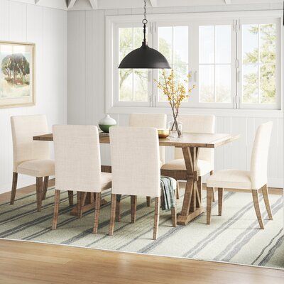 This 7-piece dining table set offers an ideal blend of classic and modern style. This set includes an extendable dining table and six chairs upholstered in a blend of cotton and linen fabric. Each piece is made with a solid pine wood frame finished in a charming light brown hue that shows off the wood's grain color variation and unique wood knots. The dining table features striking cross-beam supports adding classic touches to the classic farmhouse-style pedestal and trestle base. Best of all, t Blonde Wood Kitchen Table, Dining Room Dark Table Light Chairs, Dining Room Table Designs, Light Wood Kitchen Table, Light Wood Dining Room Table, New Classic Dining Room, Light Brown Table, Modern Farmhouse Dining Table, Light Wood Kitchens