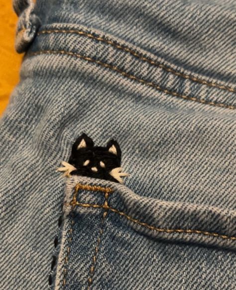 A black cat with white eyes and whiskers embroidered into jeans Diy Clothes Embroidery Ideas, Needle Point Jeans, Embroidery On Jumper, Easy Embroidery Designs By Hand, Cute Stitches On Clothes, Fun Embroidery Patterns, Hand Embroidery Jean Jacket, Embroidery With Beads On Clothes, Embroidered Jeans Diy Simple