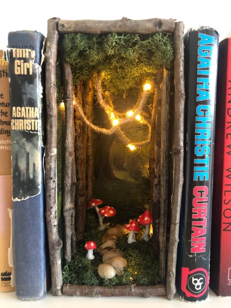 A book nook shelf insert that gives the illusion of a miniature fairy forest with mushrooms and a pebbled path between your books. Bookcase Fairy House, Book Nook Insert Diy, Fairy Inspired Decor, Diy Bookshelf Nook Insert, Fairycore Bookshelf, Book Nook Ideas Forest, Diy Forest Book Nook, Fairy Core Bookshelf, Diy Book Shelf Decor