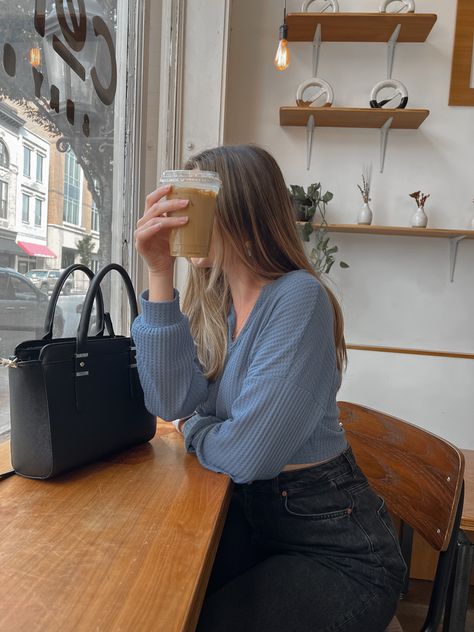 She is sitting inside a coffee shop next to the window with an iced coffee in front of her face. She is wearing a blue long sleeve cropped top with black high waisted jeans. Coffe Shoot Photo Ideas, Photography Poses Coffee Shop, Coffee Shop Pictures Photo Ideas, Coffee Shop Pose Ideas, Coffee Shop Pics Instagram, Photo Ideas In Coffee Shop, Instagram Post Ideas Coffee Shop, Coffee Cup Pictures Instagram, Insta Photo Ideas Coffee