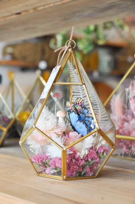 a five sided glass aerium with gold edging, filled with dried flowers and a butterfly Color Palette Pink Blue, Botanical Color Palette, Floral Outdoor Wedding, Butterfly Terrarium, Outdoor Wedding Centerpieces, Butterfly Wedding Decorations, Fairy Terrarium, Butterfly Centerpieces, Sweet 15 Party Ideas