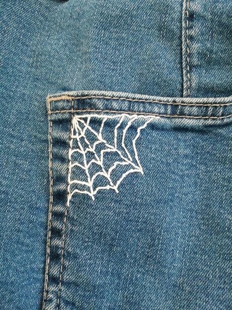 A white spider web embroidery on blue jeans pocket Jeans Stitching Ideas, Embroidery On Jeans Tutorials, Battle Vest Embroidery, Easy Things To Embroider On Jeans, Fashion Design Embroidery, Sewing Designs On Jeans, Embroidery Pants Design, Embroider Spider Web, Embroidery In Pants