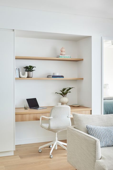 Inner-city apartment renovation showing a study nook built next to custom white joinery. The study nook features a pale timber floating desk with drawers & open timber shelving above. The shelves are styled with books, plants & ceramic items. A white office chair also sits at the desk behind an open laptop. The edge of a pale grey sofa with a blue patterned cushion and blue-grey throw can be seen in the foreground. The master bedroom, in similar tones of blue, can be seen just out of frame. Built In Office Nook In Living Room, Study In Lounge Room, Hamptons Study Nook, Linen Cupboard Study Nook, Desk Alcove Built Ins, Study Nook In Kitchen, Study Nook In Bedroom, Study Nook In Living Room, Office Nook In Living Room