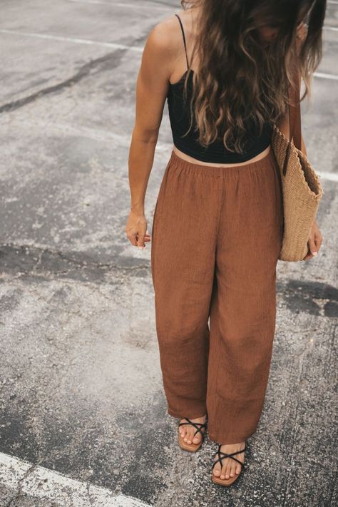 ashley wearing a black cropped cami, brown loose fitting tapered pants, black strappy sandals, and a woven tote bag walking through a parking lot Feminine Hipster Style, Modern Boho Fashion Winter, Boho Minimal Outfit, Black And Brown Outfit Summer, Black Linen Top Outfit, Brown Pants Black Top Outfit, Brown Linen Pants Outfit Summer, Brown Pants Summer Outfit, Nuetral Pallete Outfits Summer