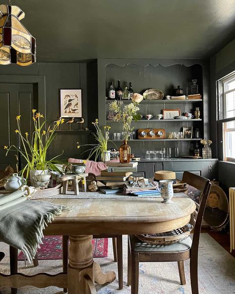 The moody aesthetic gets a refreshing transformation in this dining room, where even the ceiling is painted a dark shade of green. Painting all walls, shelving, and trim the same color is one way to achieve a seamless design. By including sturdy wooden furniture, you will encourage a distinguished look that is infused with warmth. Green Dining Room Walls, Moody Dining Room, Green Dining Room, Moody Aesthetic, Green Painting, Shade Of Green, Industrial House, Dining Room Walls, The Ceiling