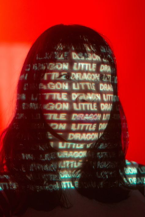 Frontwoman Yukimi of the band Little Dragon standing front of a red backdrop. The Words "Little Dragon" are projected on her face Photography Projector Background, Photo Shoot With Projector, Projector On Face, Pandora Photoshoot, Photoshoot With Projector, Creative Photo Editing Ideas, Technology Photoshoot, Cheap Dopamine, Projector Photoshoot Background