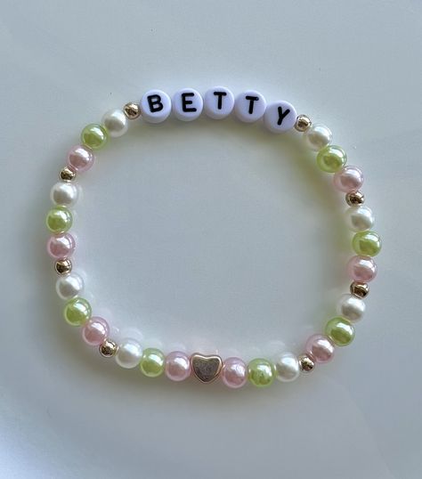 A white, pastel pink, and pastel green friendship bracelet, dotted with rose gold seed beads and a rose gold feature heart bead. The bracelet reads "Betty". Bettys Garden Bracelet, Pastel Bead Bracelet, Betty Friendship Bracelet, Betty Bracelet Taylor Swift, Friendship Bracelet Ttpd, All Too Well Bracelet, Ts Friendship Bracelets, Betty Bracelet, Bejeweled Bracelet