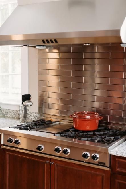 A sleek stainless steel subway tile backsplash is a nice complement to the stainless steel cooktop in this transitional kitchen. Stainless Steel Subway Tile, Copper Stove, Stainless Steel Kitchen Backsplash, Metal Backsplash Kitchen, Wood Kitchen Backsplash, Backsplash Herringbone, Kitchen Steel, Hgtv Kitchens, Farmhouse Kitchen Backsplash