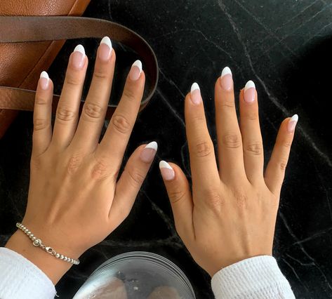 two hands stretched above a black countertop with almond shaped french tip acrylic nails. the corner of a leather bag is visible on the left side of the photo, and the base of a drink can be seen between the girls wrists. Summer Acrylic Nails French Tips Almond, Almond Shaped White French Tip Nails, Deep White French Tip Nails Almond, Glossy White French Tip Nails, Natural Acrylic Nails Almond French Tip, Coffin Acrylic Nails White French Tip, Short White Nails Almond Shape, Cute French Tip Nails Almond Shape, White French Too Acrylics