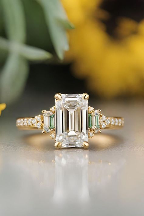 Securing the tenth position in our compilation of 21 Emerald Cut Engagement Rings, the Emerald Cut Diamond Ring with Baguette & Round Diamond Accents in Yellow Gold Pave Band epitomizes sophistication and luxury. Featuring a dazzling emerald cut diamond adorned with baguette and round diamond accents on a yellow gold pave band, this ring is a perfect blend of classic elegance and modern flair. Click to explore further and immerse yourself in the timeless beauty of this exquisite piece. Emerald Cut Engagement Ring Gold Halo, Emerald Engagement Ring Tapered Baguette, Engagement Ring Classic Elegant, Emerald Cut Engagement Ring With Accents, Emerald Baguette Ring Engagement, Emerald Cut Engagement Ring Art Deco, Wedding Rings With Baguettes, Emerald Cut Engagement Ring With Baggets, Wedding Band Emerald Engagement Ring