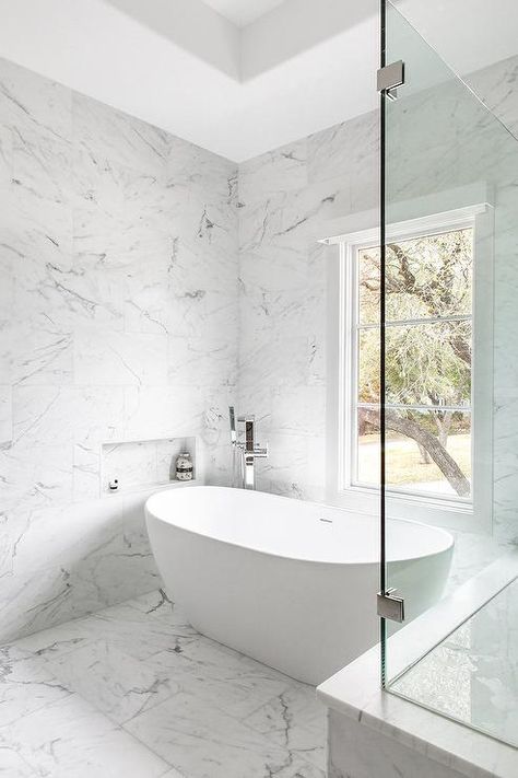 A marble tiled niche, surrounded by marble wall tiles, is positioned above an oval freestanding bathtub paired with a polished nickel modern floor mount tub filler and placed on marble floor tiles beneath a window. Tiled Niche, Bathroom Tub Remodel, Austin Interior Design, Tub Remodel, Bathroom Freestanding, Marble Tile Bathroom, Marble House, Marble Wall Tiles, Marble Tile Floor