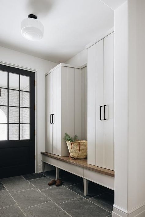 Fixed against slate floor tiles, a wood top mudroom bench is positioned under white plank locker cabinets adorned with oil rubbed bronze pulls lit by a milk glass schoolhouse semi flush mount. Slate Floor, Kate Marker Interiors, Slate Tile Floor, Mudroom Lockers, Cabinetry Hardware, Farrow And Ball Paint, Slate Flooring, Wicker Decor, Slate Tile