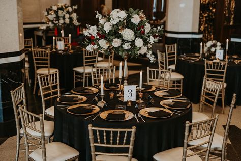 Modern Wedding Reception that takes you back to a different time - Gold Chaivari Chairs, Gold Chargers, Black Table Linens, with Tall Floral Centerpieces and Taper Candles in a Historic Venue - Wedding Table Decor - Wedding Reception Decor #dallasweddingplanner #dallaswedding #dallasweddings #weddingplanner #weddingplanning #weddingdetails #planner #texasweddingplanner #texaswedding  #txweddings #txwedding #wedding #weddingday #weddinginspiration #engagement #proposal  #realwedding Wedding Reception Black And Gold, Black Linen Gold Charger, Black And Gold Wedding Reception Tables, Wedding Table Decorations Black And Gold, Black Gold Table Decorations, Black Linen Wedding Table Centerpieces, Gold And Black Wedding Centerpieces, Dark Table Linens Wedding, Black Gold And Ivory Wedding Table Settings