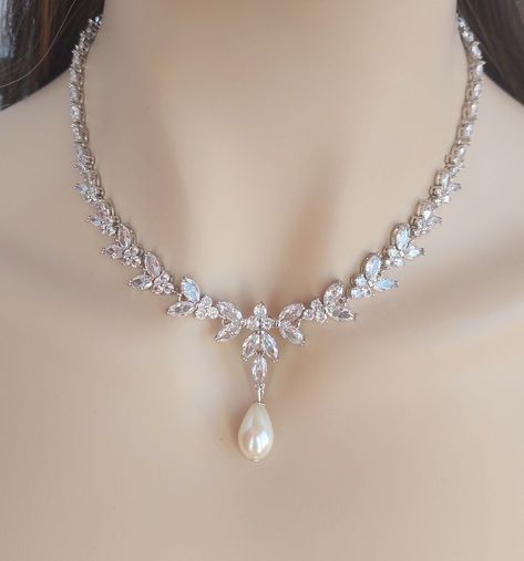 ❤️ Best seller! Luxurious and eye catching V shape bridal necklace (and earrings optional) designed to be delicate and feminine. This bridal necklace is made with marquise cut, clear Cubic Zirconia in silver-platinum plated \settings forming a floral, leaf motifs. This timeless jewelry is very elegant and sparkles beautifully catching and reflecting the light. - Necklace length: 17 inches long (please, contact me for a longer necklace) The necklace closes with an easy to manipulate silver plated foldover clasp. *The necklace can also be made without the CZ drop dangling bellow. - Earrings length: 30mm longme and dangle from CZ set stud ear posts. Matching bracelet: https://www.etsy.com/listing/859475493/silver-bridal-bracelet-crystal-wedding?ref=listing_published_alert https://www.etsy.com Vintage Wedding Necklace, Necklace Ideas Silver, Light Necklace Designs, Pearl Sets Jewellery, Winter Wedding Jewelry, Pearl Wedding Jewelry Sets, Prom Necklace, Bridal Jewelry Pearl Sets, Silver Bridal Jewellery