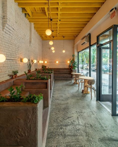 The furniture is positioned against exposed brick walls that are painted white in contrast to the cafe's bright yellow ceiling. Stepped Seating, White Brick Interior, Brick Restaurant, Yellow Restaurant, Brick Cafe, Restaurant Exterior Design, Painted Brick Exteriors, Cafe Exterior, Small Staircase