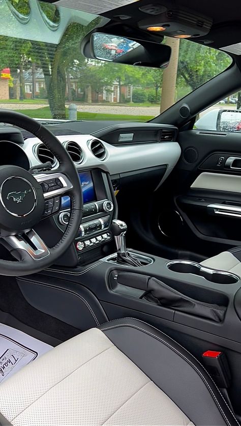 Interior of a 2022 Ford Mustang GT Coupe Premium with light and dark dual-toned interior seating parked at Bill Brown Ford in Livonia, Michigan. Surrounding the vehicle is green grass and a tree, which can be seen through the front windshield. Coupe, Mustang Interior Aesthetic, 2022 Mustang Gt, White Interior Car, Ford Mustang Gt Interior, Mustang Gt Interior, 2022 Mustang, Mustang Steering Wheel, Ford Mustang History