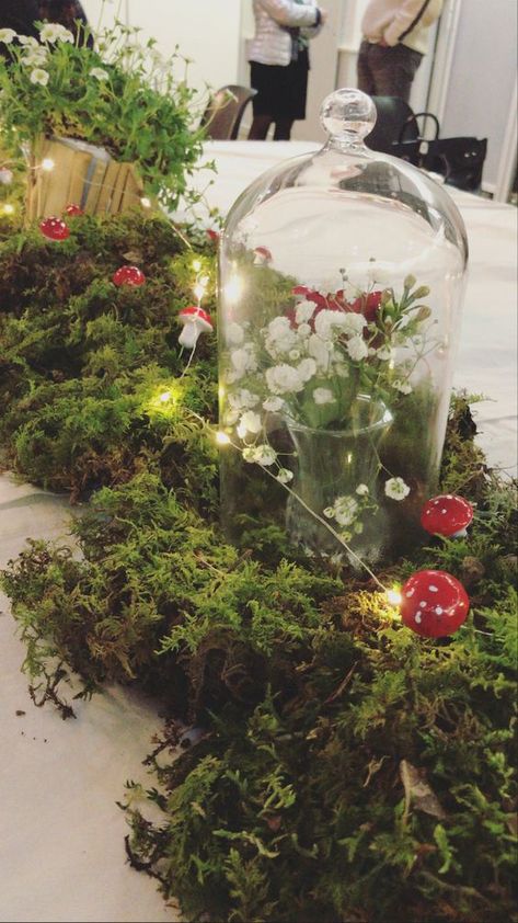 an enchanted forest wedding centerpiece of moss, lights, mushrooms, a cloche with white blooms is a lovely decoration to compose Enchanted Forest Floral Arrangements, Enchanted Themed Party, Vine Party Decor, Enchanted Forest Party Decor, Fairy Wonderland Birthday Party, Woodland Quinceanera Theme, Shrek Wedding Theme, Enchanted Forest Theme Decorations, Enchanted Forest Wedding Centerpieces